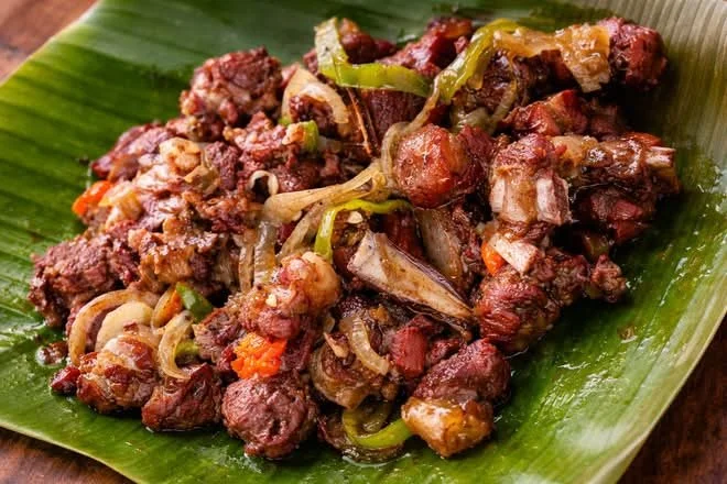 Ntaba grillé aux oignons et poivrons servi sur une feuille de bananier
